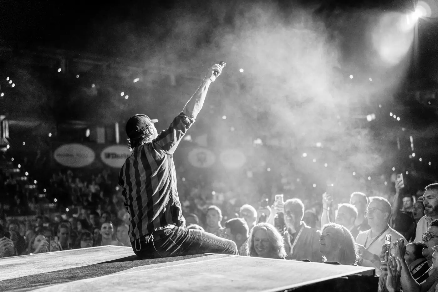 Dierks Bentley sitting at the edge of the thrust stage over the crowd, black and white