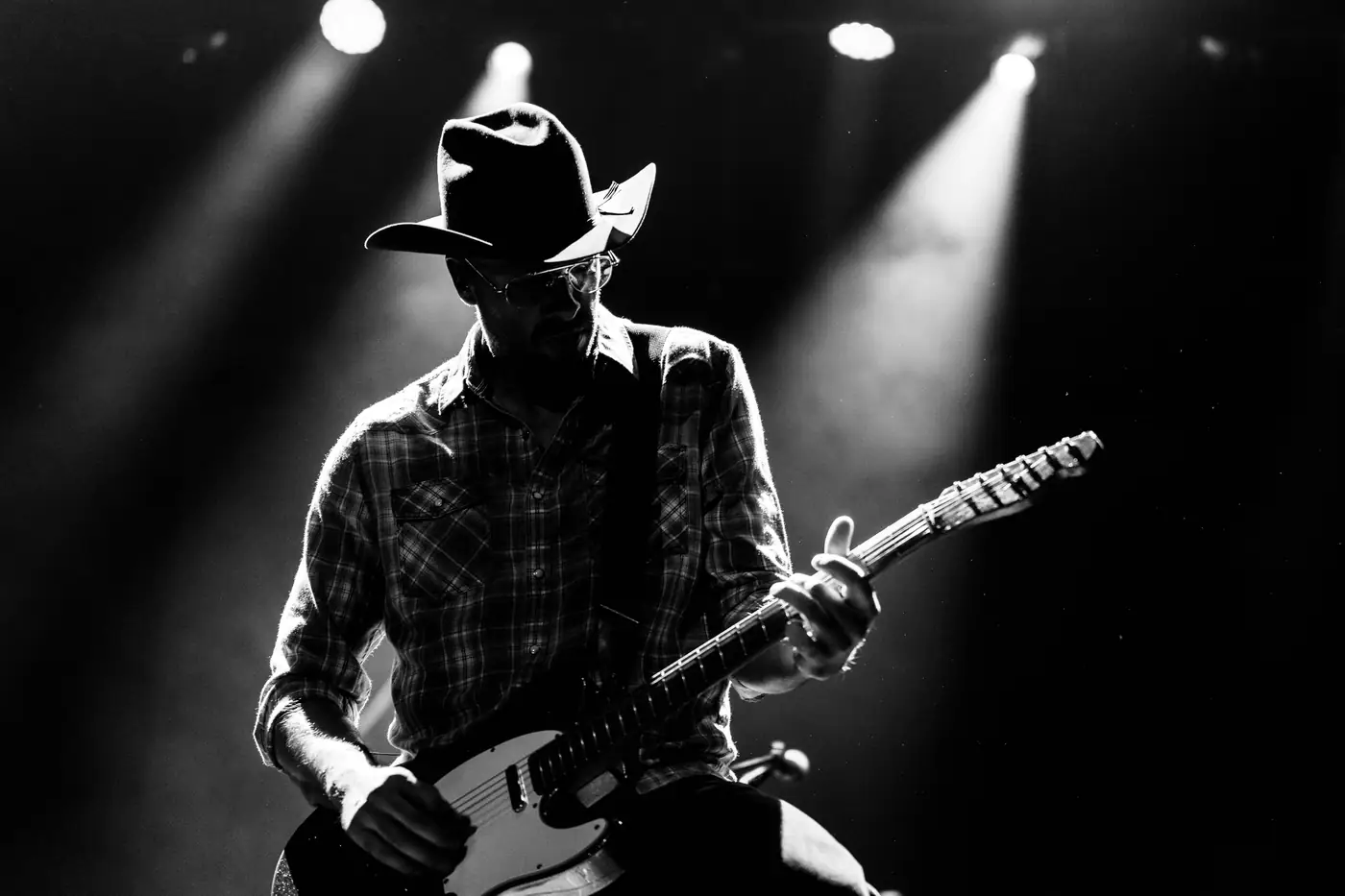 Guitarist in a cowboy hat backlit by stage spots, black and white