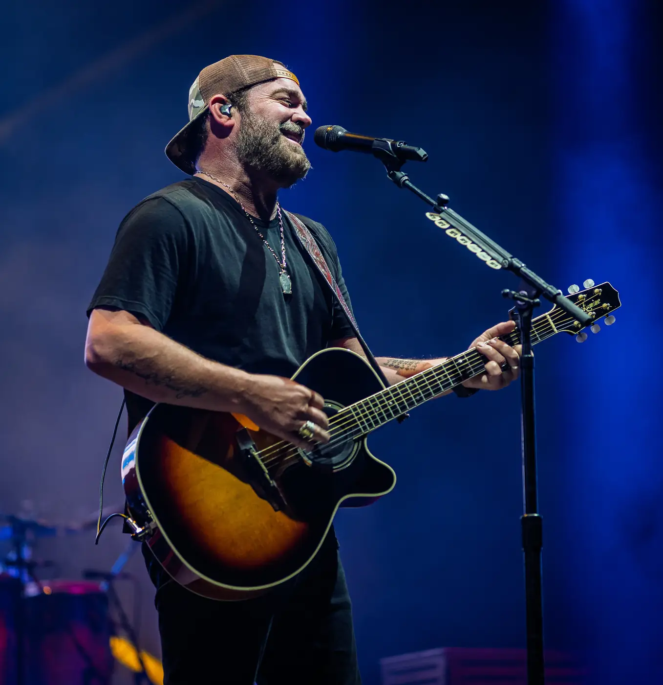 Lee Brice smiling at the microphone with acoustic guitar in blue light