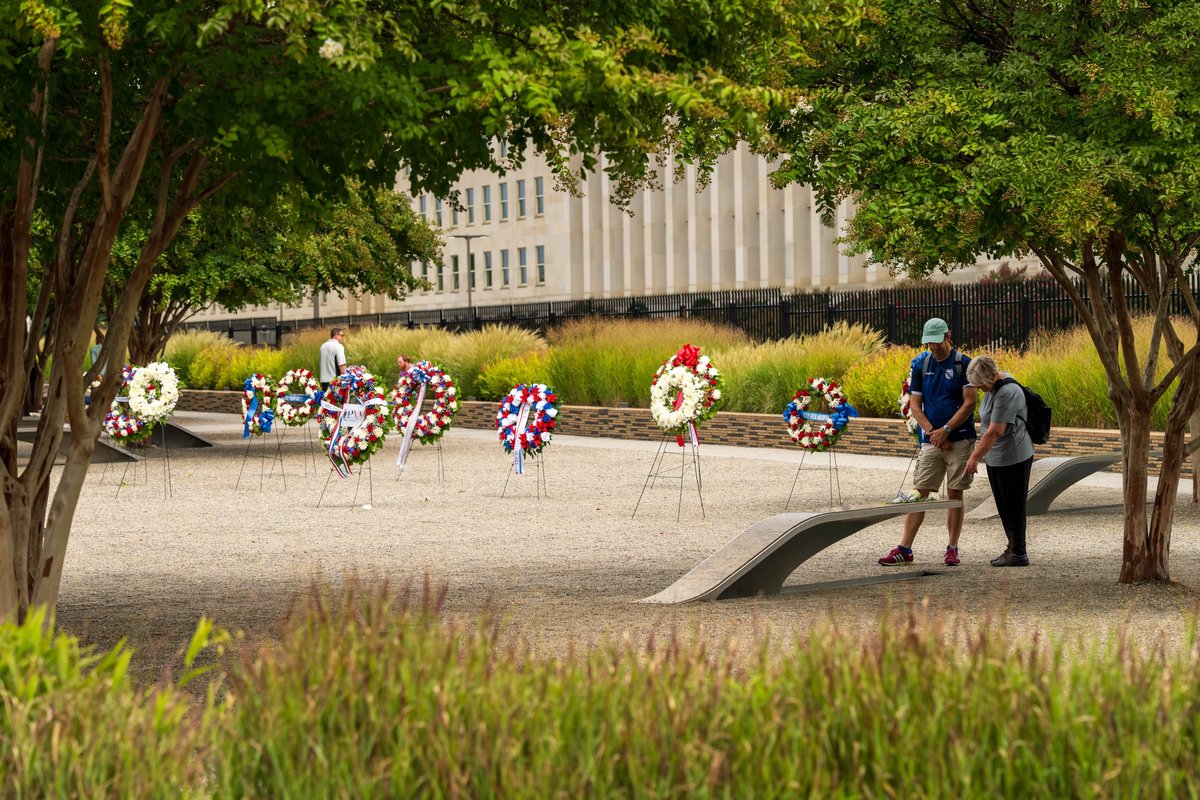 Wreaths on easels at the National 9/11 Pentagon Memorial, with the flag hanging on the Pentagon behind them